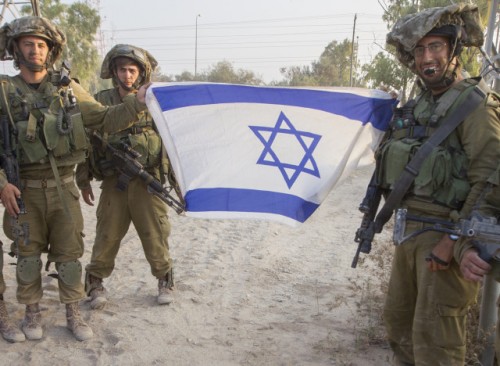 Israeli soldiers pose with a national flag upon their return from combat in the Gaza Strip at an army deployment area near Israel's border with the besieged Palestinian territory on July 23, 2014, as the conflict entered its third week with neither side showing any sign of willingness to pull back. Israel's military pursued a relentless campaign of shelling and air strikes while the Palestinian militants hit back with rocket fire and fierce attacks on troops operating on the ground. Around 650 Palestinians and 29 Israeli soldiers have been killed in the Gaza fighting which began on July 8.  AFP PHOTO / JACK GUEZ