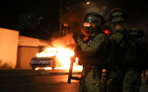 Israeli security force members stand near a burning Israeli police car during clashes between Israeli police and members of the country's Arab minority in the Arab-Jewish town of Lod, Israel May 12, 2021. REUTERS/Ammar Awad