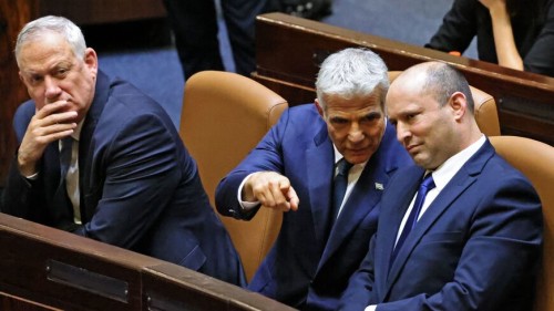 (L to R) Israel's Defence Minister Benny Gantz looks on while Alternate Prime Minister and Foreign Minister Yair Lapid converses with Prime Minister Naftali Bennett as they are seated in the Knesset chamber after a special session to vote on a new government at the Knesset in Jerusalem, on June 13, 2021. - Featuring Israeli political veterans and a record number of female lawmakers, a motley coalition including two left, two centre, one Arab Islamist and three right-wing parties came to power Sundayin an eight-party alliance united by animosity for outgoing prime minister Benjamin Netanyahu. (Photo by EMMANUEL DUNAND / AFP) (Photo by EMMANUEL DUNAND/AFP via Getty Images)