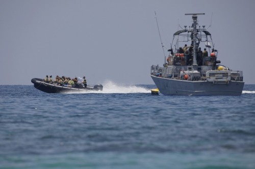 People sail past an Israeli navy vessel off the coast of Rosh Hanikra, an area at the border between Israel and Lebanon (Ras al-Naqura), on June 6, 2022. - Tensioned flared between the two nations after a new Israeli gas drilling rig entered the disputed maritime borders, in a move the Lebanese labelled as an act of aggression and a provocation. (Photo by JALAA MAREY / AFP)