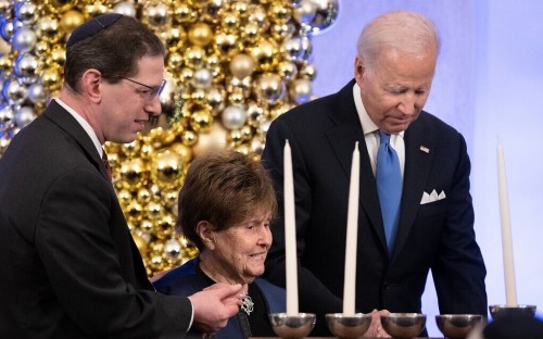 Rabbi Charlie Cytron-Walker and US President Joe Biden help Holocaust Survivor Bronia Brandman to a menorah during a Hanukkah Holiday Reception in the Grand Foyer of the White House in Washington, DC, December 19, 2022. (Photo by Brendan Smialowski / AFP)